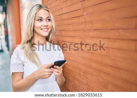 Young caucasian girl smiling happy using smartphone leaning on the wall.