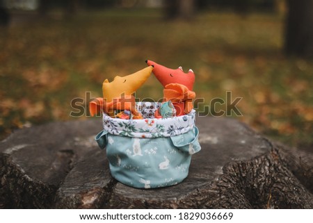Cute little handmade toys sit in a basket in the autumn garden. Childhood, baby, holiday, people, hobby, emotions concepts.