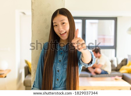 young pretty asian woman feeling proud, carefree, confident and happy, smiling positively with thumbs up