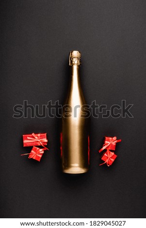 Top view of golden champagne bottle near toy gift boxes on black background