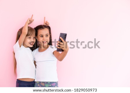 people, children, technology, friends and friendship concept - happy little girls with smartphones lying on floor at home education, school are using a smartphone and smiling