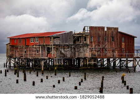 Worn down dilapidated wooden cannery on the Columbia River in Astoria, Oregon, on a cloudy moody darkening sky evening. Royalty-Free Stock Photo #1829052488