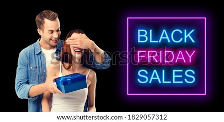 Love, dating, celebrating, lovers concept - happy amorous couple with blue gift box. Isolated over dark background. Black friday sales neon light sign text.14 february, valentine holiday, Valentin day