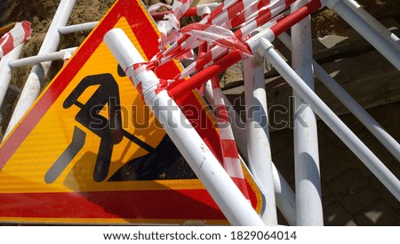 Road works sign denoting construction work and metal fencing on the ground. Close up. Red and yellow сolour. Restoration and reconstruction concept. Traffic barrier. Providing security control. 