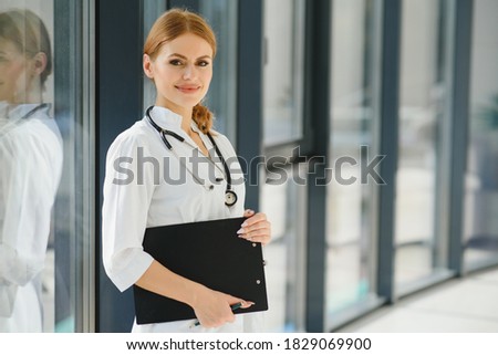 Portrait of attractive female doctor holding clipboard while standing in clinic