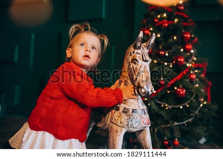 Little baby girl by Christmas tree with wooden toy