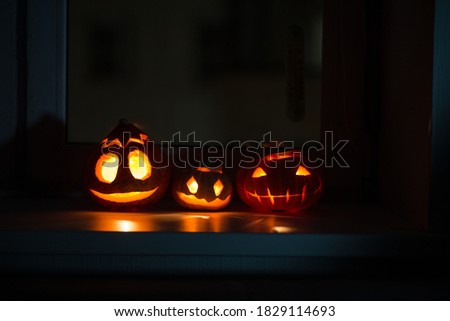 Three different glowing halloween pumpkins on a windowsill against a background of maple leaves at night