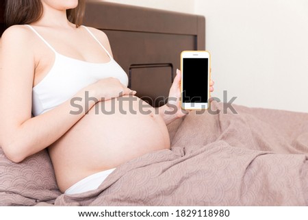 Cropped shot of pregnant woman showing smartphone with black screen in bed.