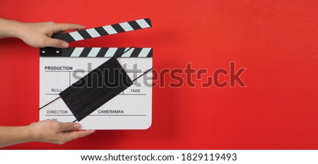 Hand is holding Clapper board or movie slate with black face mask. it use in video production and cinema industry on red background.