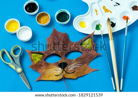 Mask painted on maple leaf. Drawing on autumn leaves. Cat Fox mask for kids autumn carnival or party. Art project for children. DIY concept