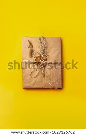Handmade gift box packed in craft paper decorated with dried flowers. on yellow backround. Template for posters and banners Flat lay photo with copy space.