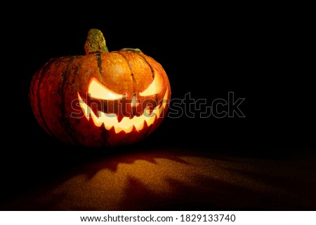 Halloween pumpkin with glowing eyes and mouth on black background with copy space
