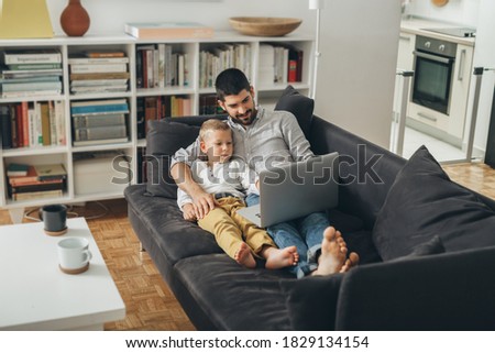 father and son laying on sofa and using laptop computer at home