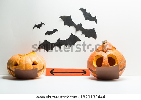 Two different Halloween pumpkins wearing medical masks stand at a safe social distance. They stand on a white background with bats. It symbolizes Halloween 2020 with covid 19 coronavirus