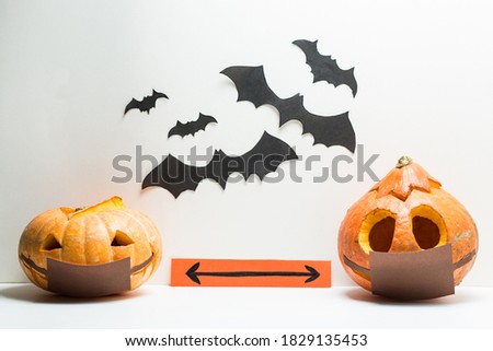Two different Halloween pumpkins wearing medical masks stand at a safe social distance. They stand on a white background with bats. It symbolizes Halloween 2020 with covid 19 coronavirus