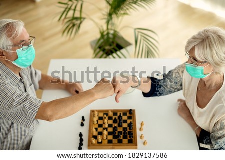Senior couple congratulating each other and fist bumping while playing chess at home during COIVD_19 pandemic. Royalty-Free Stock Photo #1829137586