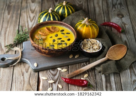 Homemade pumpkin cream soup with seeds, spices and herbs on a rustic background.