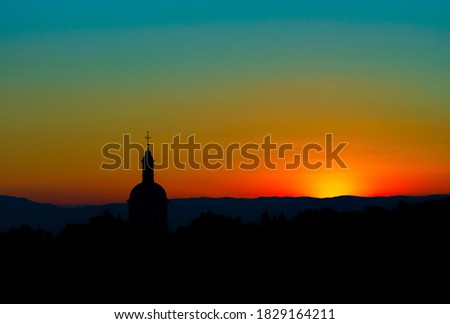 The stunning beauty and colors of the sunset overlooking the silhouettes of the Alps and the silhouette of a beautiful church in the foreground. Geometry and graphics, panorama. Cover or screen saver.