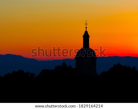 The stunning beauty and colors of the sunset overlooking the silhouettes of the Alps and the silhouette of a beautiful church in the foreground. Geometry and graphics, panorama. Cover or screen saver.