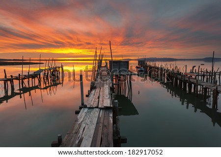 Red Sky Fire Sunset in the old port of artisanal fishing. The Carrasqueira Pier is a tourist destination in Alentejo, near Lisbon. Royalty-Free Stock Photo #182917052