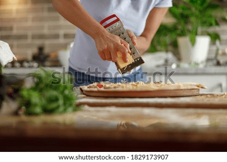 Beautiful smily handsome woman is preparing tasty fresh italian pizzawith vegetables at her kitchen at home