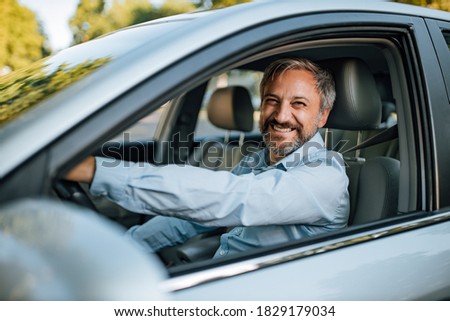 An older man smiling in the camera while he prepares to drive a car. Royalty-Free Stock Photo #1829179034