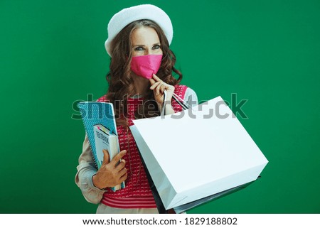 Life during coronavirus pandemic. pensive trendy female in pink sleeveless shirt with textbooks, notebooks, pink medical mask and shopping bags looking at copy space on green background.