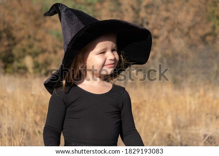 cute toddler girl in black witch hat in nature.