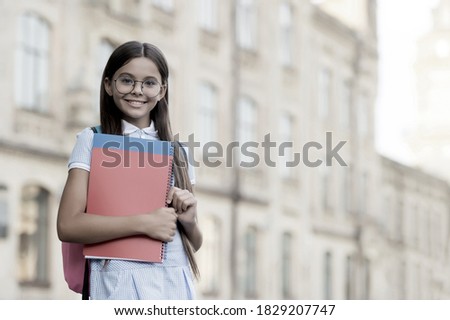 Happy smart kid wear glasses back to school carrying backpack and books at education building outdoors vintage filter, retro, copy space.