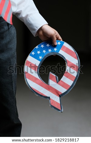 Qanon "Save children" concept. Unrecognisable child holding in his hand Q letter with american flag. Concept image for banned movement in the Untied States of America.