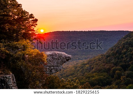 The sun rises over Whitaker Point, known as Hawksbill Crag, in Arkansas as the fall colors begin to set in on the trees Royalty-Free Stock Photo #1829225615