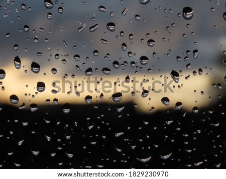 Raindrops on window and dramatic sunset and black - white rain clouds. Background blurred