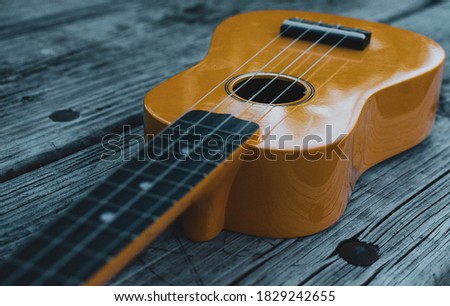Old fation photo of yellow ukulele in the wethered table