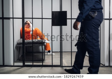 A prison guard makes a tour of the cells in a high-security prison. The cells are occupied by criminals in red robes Royalty-Free Stock Photo #1829267459