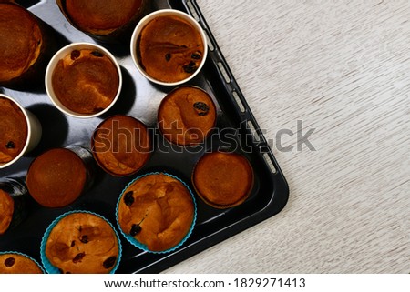 Easter cakes, crispy brown, with raisins, in small various round shapes. On the black oven tray, on the left, is a fragment of the corner. Baking result.