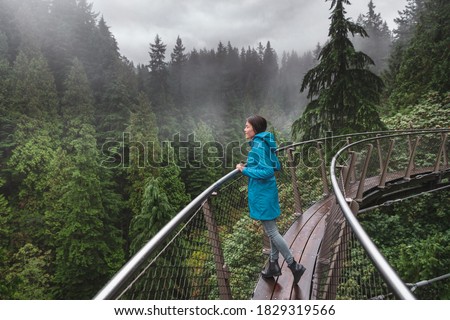 Canada Autumn travel destination in British Columbia. Asian tourist woman walking in famous attraction Capilano Suspension Bridge Park in North Vancouver, canadian vacation for tourism. Royalty-Free Stock Photo #1829319566