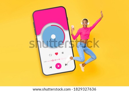 Fun energetic African American woman wearing headphones listining to music from application in smartphone on colorful yellow isolated background