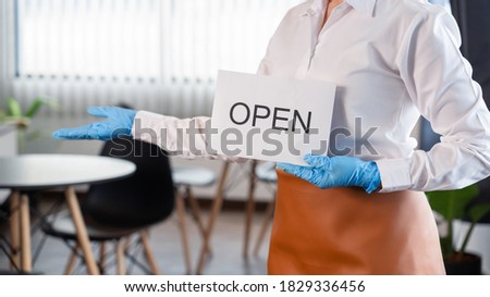 Happy waitress with protective face mask holding open sign for the reopening at her restaurant after lockdown the quarantine coronavirus or covid-19 adapt to new normal 