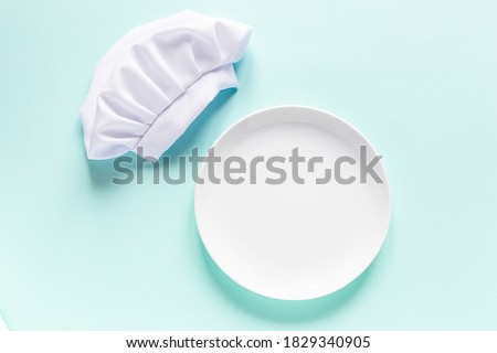 White empty plate with copy space for yout text and chef cap above. Cooking menu preparation Royalty-Free Stock Photo #1829340905