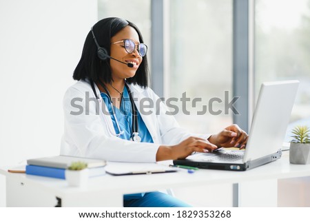 African doctor wear headset consult female black patient make online webcam video call on laptop screen. Telemedicine videoconference remote computer app virtual meeting. Over shoulder videocall view. Royalty-Free Stock Photo #1829353268