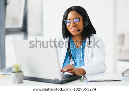 African doctor wear headset consult patient make online webcam video call on laptop screen. Telemedicine videoconference remote computer app virtual meeting. Over shoulder videocall view. Royalty-Free Stock Photo #1829353274