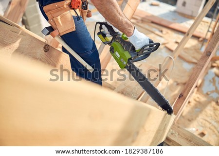 Cropped photo of a skilled worker using a chainsaw cutting machine on pieces of building timber