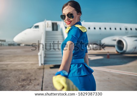 Waist up portrait of joyful beautiful young woman in uniform and sunglasses walking to stairway before flight Royalty-Free Stock Photo #1829387330