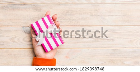 Girl Hands holding craft paper gift box with as a present for Christmas or other holiday on yellow rustic wooden background, top view with copy sppace.