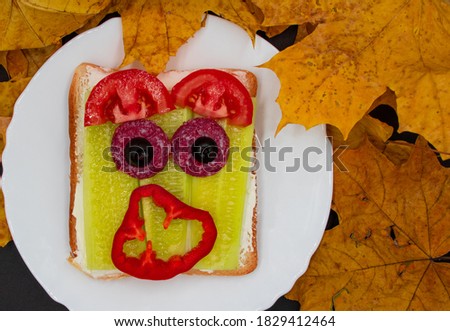 Funny halloween monster sandwich with slice of sausage, cucumber, bell pepper and tomatoes on a plate and with autumn leaves Royalty-Free Stock Photo #1829412464