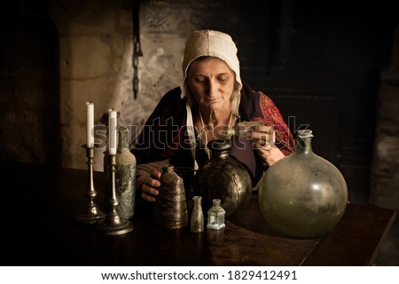 Woman in medieval outfit working as an alchemist or witch in the kitchen of a French medieval castle