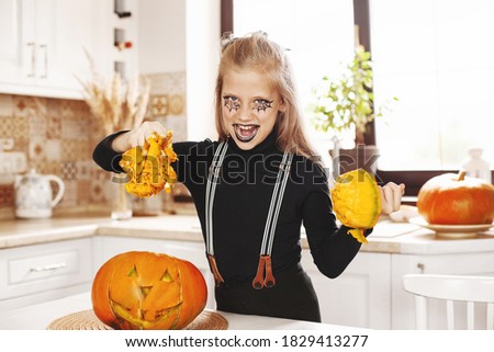 Happy little girl in costume and holiday makeup with scary look at halloween party with big pumpkin