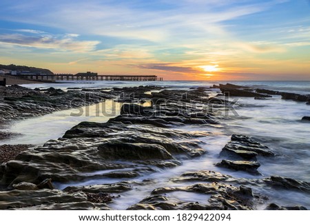 The sun rising and the tide receding revealing the rocks on St Leonards beach with Hastings pier on the horizon, east Sussex south east England Royalty-Free Stock Photo #1829422094
