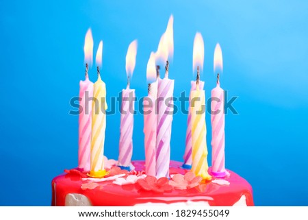 White cream cake with red icing and a candle on a blue background. Birthday concept.