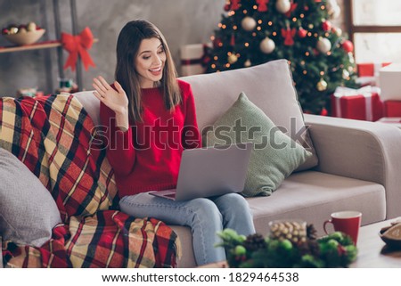 Photo of young pretty lady sit couch hold computer waving arm wear red pullover jeans in decorated x-mas living room home indoors